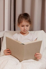 Wall Mural - portrait of little girl sitting in bed and reading book