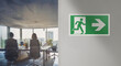 © Rioji - Right emergency exit sign installed on the wall of a modern office blurred in the background. Space for text insertion. Image with warm tones and colors.