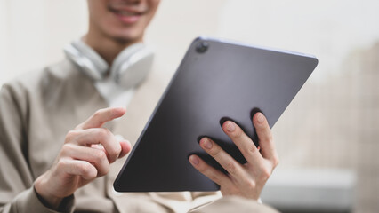 Poster - A man is sitting on a chair and holding a tablet. He is smiling and he is enjoying his time, Close-up on hands holding tablet