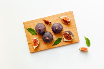 Canvas Print - Plate with fresh ripe figs whole and slices with green leaves on wooden cutting board. Top view