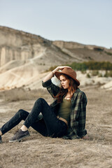 desert wanderlust woman in plaid shirt and hat relaxing on ground in arid landscape