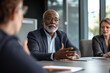 © wolfhound911 - A senior Black executive engages in a discussion about risk transfer strategies led by a middle-aged Caucasian team leader. The meeting room is modern, with visual aids and a round table promoting