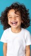 © ABDULHAMID - a happy, laughing child with curly hair, wearing a white t shirt against a blue background