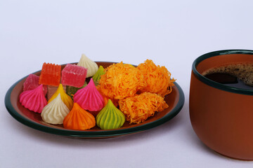 Crispy desserts of many colors and shapes arranged in a brown plate with green edges. and black coffee in the same color cup placed on a white background