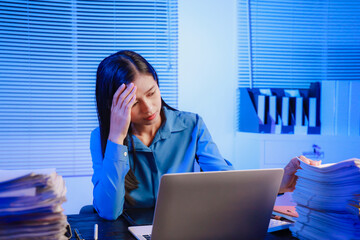 Asian businesswoman working hard in front of computer and many documents on desk at office late at night with serious action