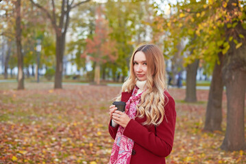 A woman in a red coat and a black skirt walks in an autumn park. The concept of autumn and the beauty of nature.