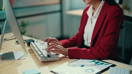 Aufkleber - Businesswoman wearing a red suit jacket is working at her desk. She is typing on a keyboard and looking at a computer screen