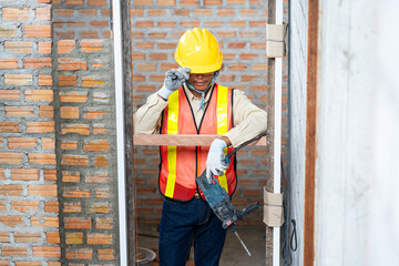 Wall Mural - A construction worker stands holding a drill at the construction site, skill and the tools essential for building projects.