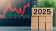 © JAKE STUDIO - Wooden blocks with number 2025 on a desk with financial graphs in background.
