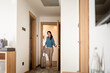 © lordn - A smiling woman enters a hotel room, pulling her suitcase behind her and holding a jacket. She looks ready to settle in, with a modern, minimalist hotel setting in the background.