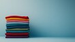 © Elmira - A tidy pile of clothes in bright colors like red, blue, green, and yellow rests against a light blue backdrop. The arrangement emphasizes cleanliness and fresh style