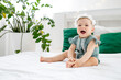 © Any Grant - little baby girl on the bed at home in a green bodysuit smiling or laughing, cute funny baby at home before going to bed, lifestyle,