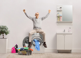 Canvas Print - Happy elderly man raising arms and sitting on a washing machine