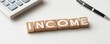 © JAKE STUDIO - Wooden blocks spelling income with calculator and pen on white background.
