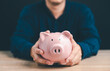 © flyalone - Man hand holding piggy bank on wood table with black background. The concept of saving money and financial investment
