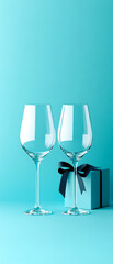 Elegant wine glasses paired with a beautifully wrapped gift box on a vibrant teal background, perfect for celebrations.