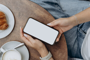 Mockup woman's hand holding using smart phone with white blank screen POV at coffee shop, mobile app design and advertising, online marketing