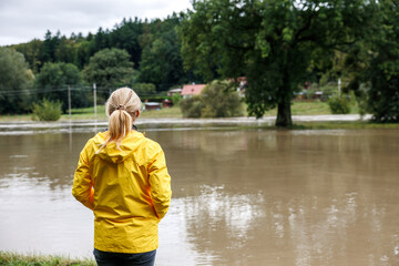 flooded river. worried woman looking at overflowing water during flood. extreme weather and natural 