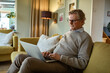© Marko Geber - Serious senior man typing on laptop from couch at home