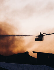 Wall Mural - Firefighters use telescopic tower during massive large blaze fire, firetruck with crane, firemen team putting out the fire with extendable fire ladder, blazing warehouse factory, burning building