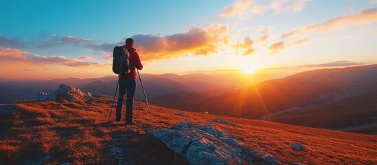 Wall Mural - a lone hiker stands on a mountain peak at sunset, gazing at the breathtaking panoramic view.