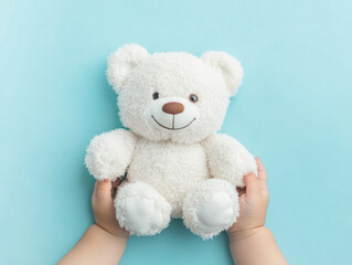 A child's gentle hands cradle a soft white teddy bear on a serene blue backdrop