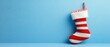 © Nathamanee - A red and white striped Christmas stocking sits on a blue wall