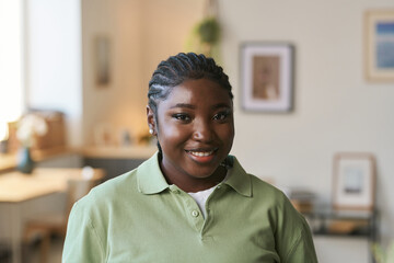 Wall Mural - Front view portrait of young Black woman wearing uniform standing in home interior and smiling at camera, copy space