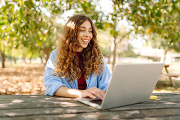 Wall Mural - Young woman brought her laptop to the park to get some fresh air and work. Online education, Freelance work, technology concept.