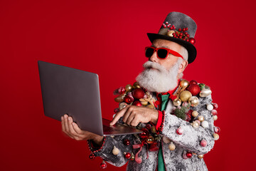 Wall Mural - Photo of santa claus funny man hold netbook typing dressed christmas tree balls costume sunglasses isolated red color background