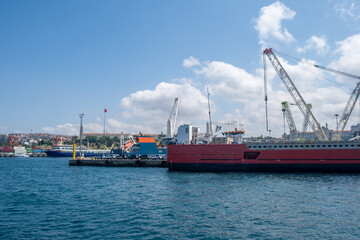 Poster - Cargo ships docked at a busy harbor with cranes and a clear blue sky in the background during midday