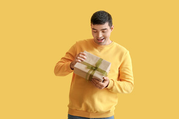 Happy young man with gift on yellow background