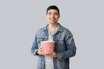 Wall Mural - Happy young man with popcorn on light background