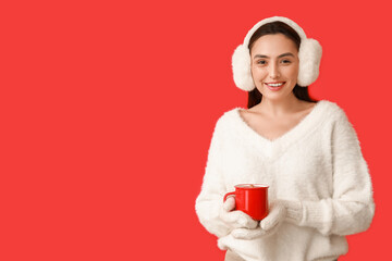 Wall Mural - Beautiful young woman in warm mittens with cup of hot mulled wine on red background