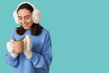 Wall Mural - Beautiful young woman in warm mittens with cup of hot mulled wine on blue background