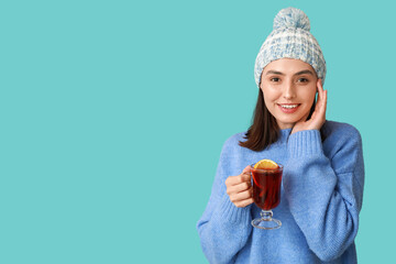 Wall Mural - Beautiful young woman with glass cup of hot mulled wine on blue background