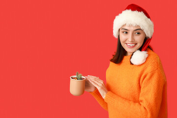 Wall Mural - Beautiful young woman in Santa hat with cup of hot mulled wine on red background