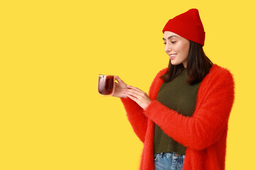 Wall Mural - Young woman with glass cup of hot mulled wine on yellow background