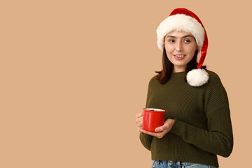 Wall Mural - Beautiful young woman in Santa hat with cup of hot mulled wine on brown background