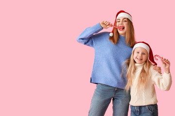 Poster - Cute little girl and her mother in Santa hats with Christmas candy canes on pink background