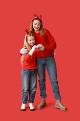 Wall Mural - Cute little girl and her mother in reindeer horns showing heart gesture on red background