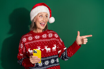 Sticker - Photo of cheerful woman wear red santa hat clothes recommend gadget empty space isolated on green color background