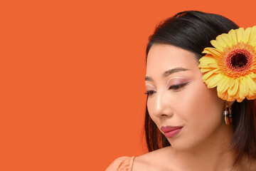 Poster - Beautiful young Asian woman with gerbera flower on orange background