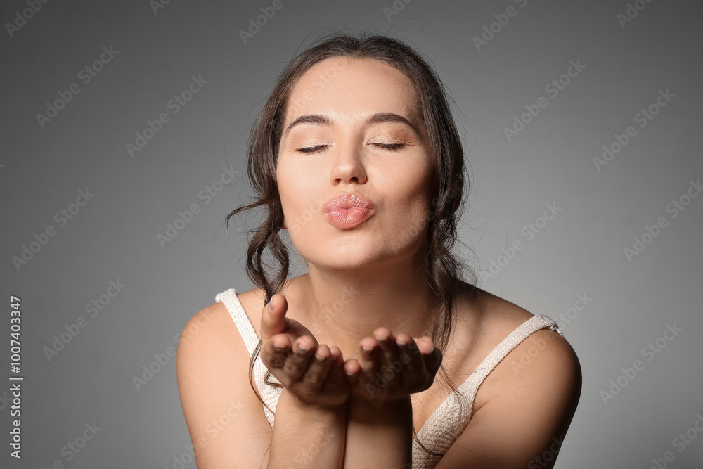 Young woman with beautiful lips blowing kiss on grey background