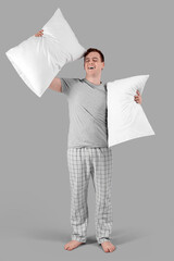 Canvas Print - Handsome young happy man in stylish pajamas with pillows on grey background