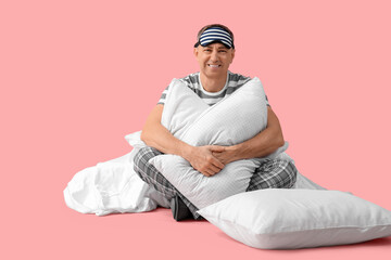 Poster - Handsome mature happy man in stylish pajamas with pillows and blanket on pink background