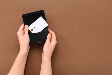 Wall Mural - Female hands with black credit card holder on brown background