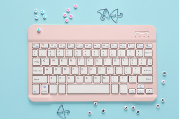 Wall Mural - Pink computer keyboard and paper clips on blue background. Top view