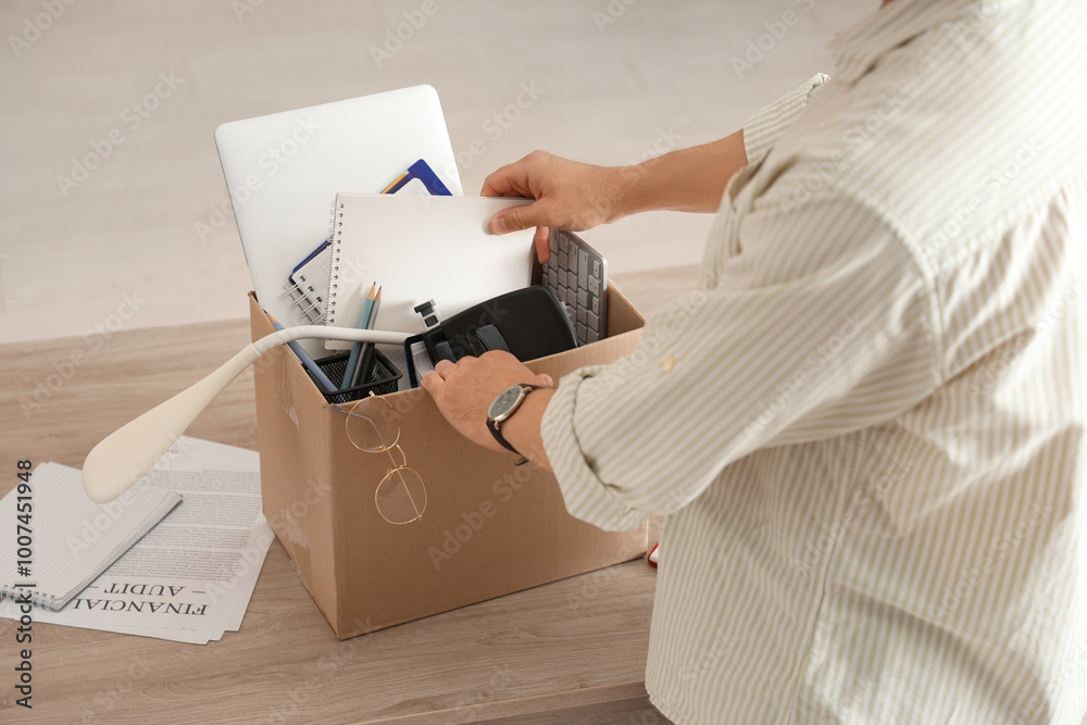 Fired young man packing his personal stuff in box on table in office, closeup