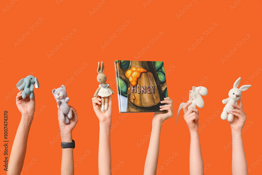 Female hands with different knitted toys and book on orange background